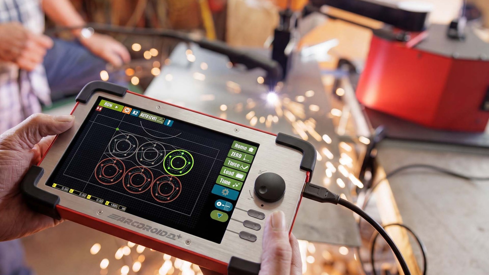Hands holding the ArcDroid Plus controller with a touchscreen showing circle cut paths and a joystick, with plasma cutting sparks in the background