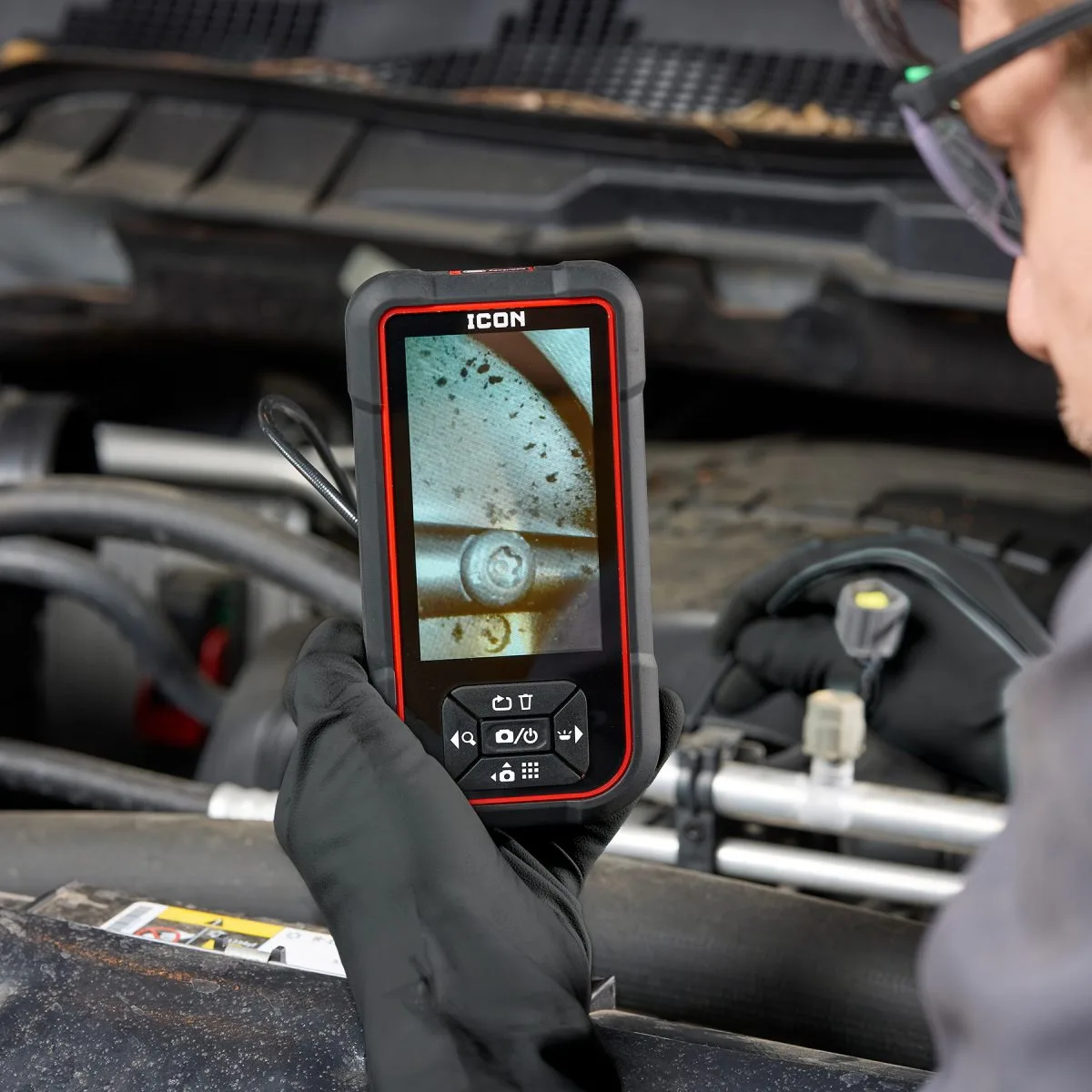 A mechanic checking the camera's live view while working in an engine bay