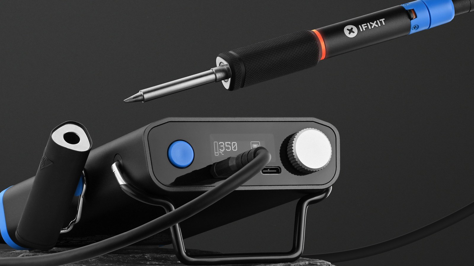 iFixit FixHub smart soldering iron resting beside its portable power station on a dark background