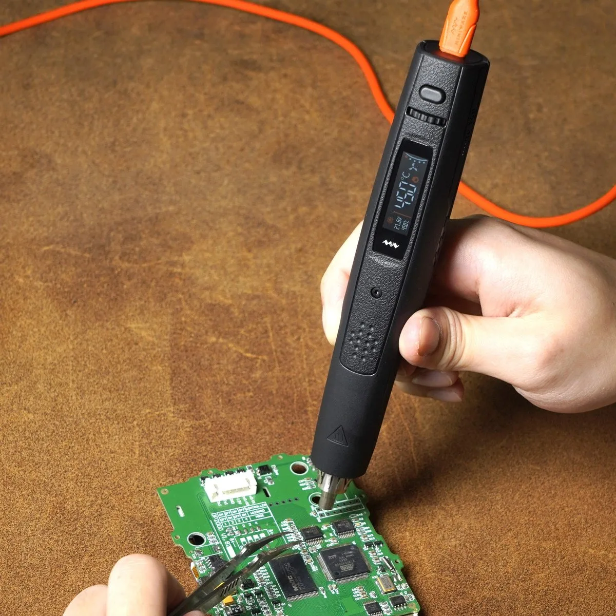 A hand holding the AirGo 140 over a circuit board while its cable trails off
