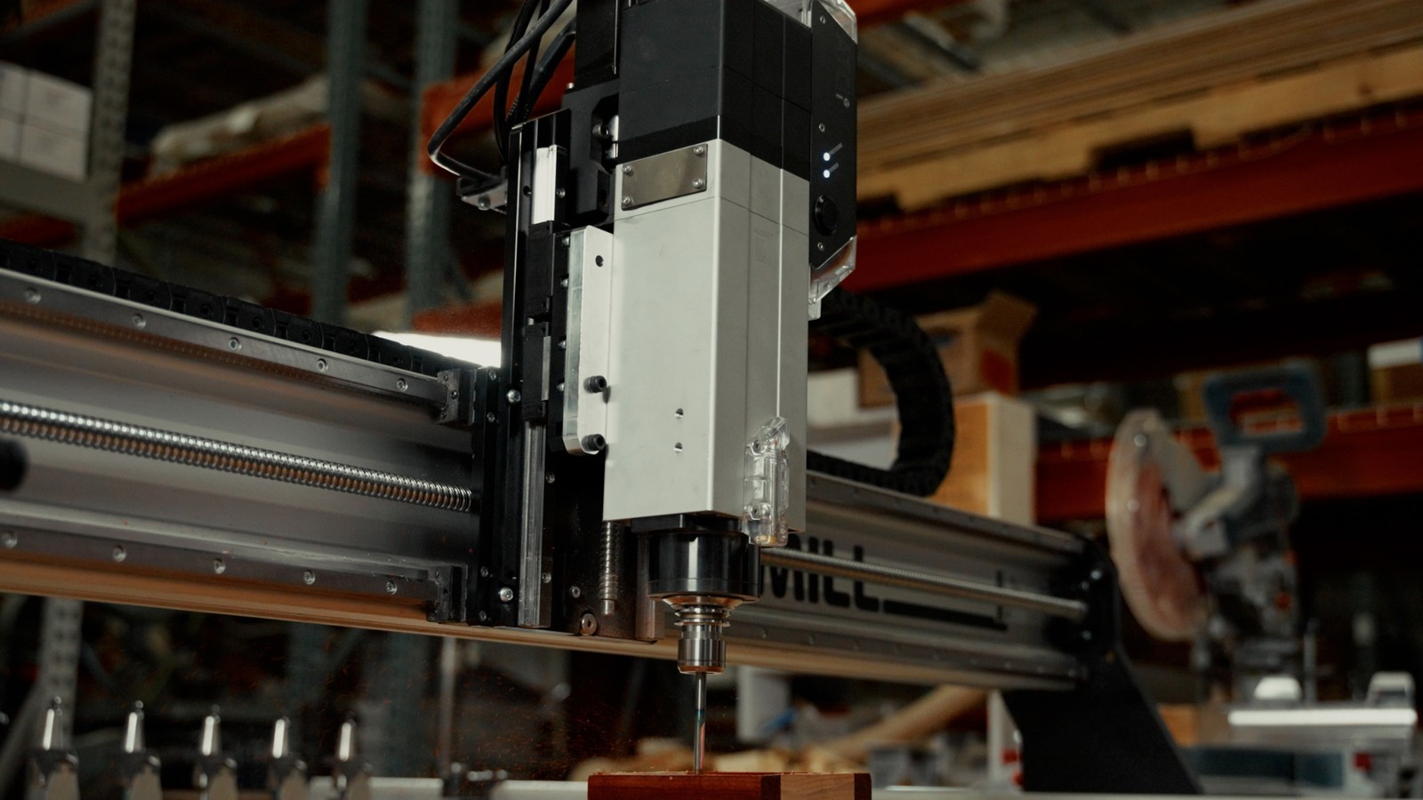 Sienci AltMill automatic tool changer spindle cutting a block of wood in a workshop, with the tool rack visible at the left