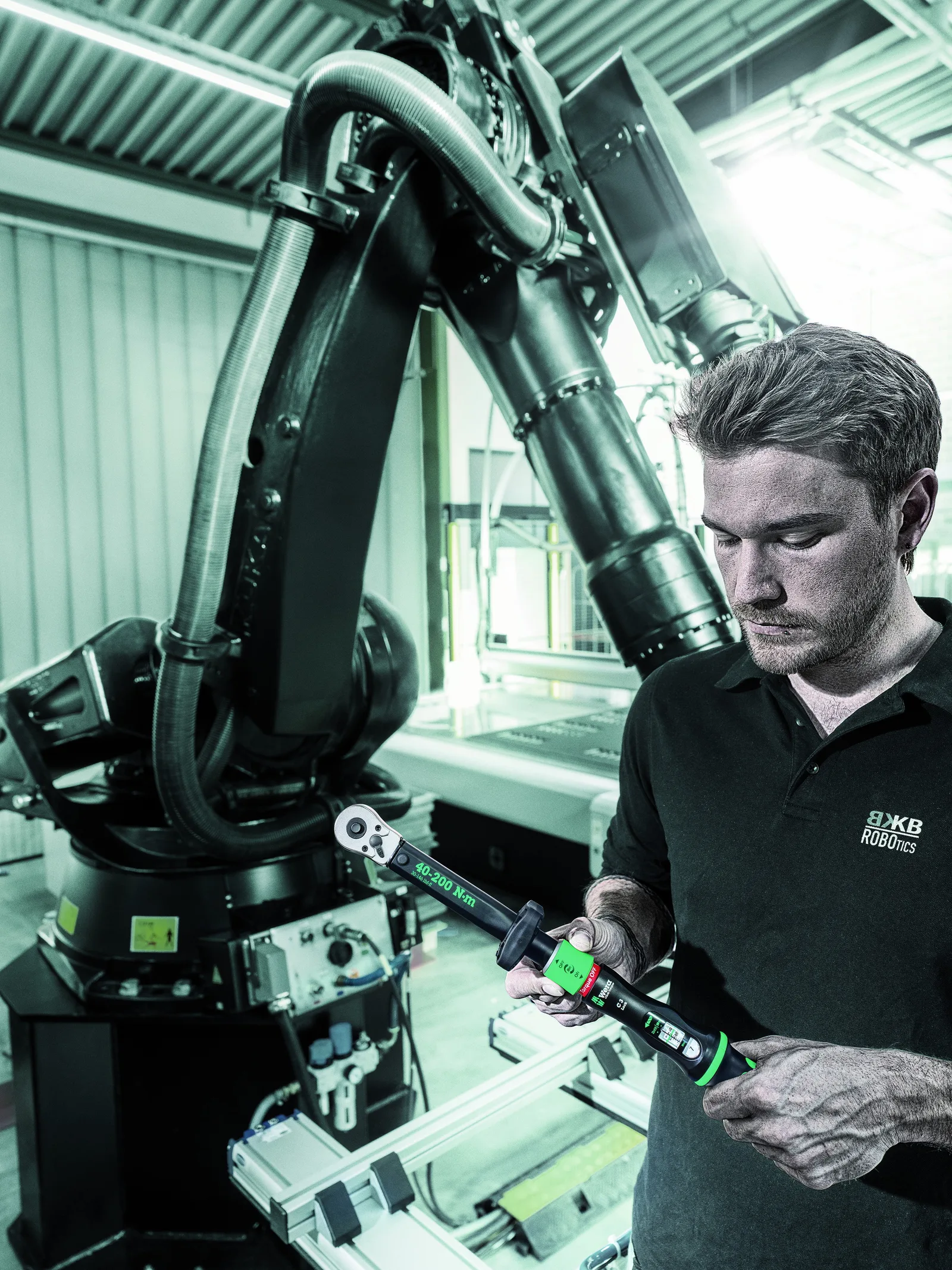 A technician using a Click-Torque wrench on a fastener beside an industrial robot arm