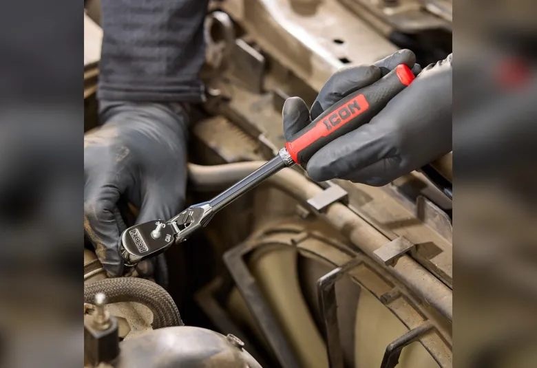 Mechanic using an ICON G2 ratchet with a red comfort grip on a fastener inside an engine bay
