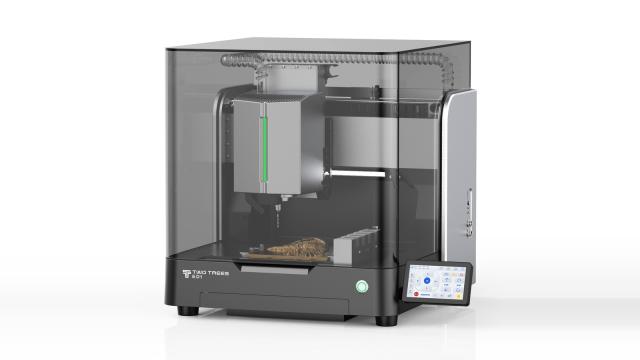 TwoTrees ED1 enclosed desktop CNC machine with a smoked glass cover, spindle and tool changer inside, a carved piece on the bed, and a touchscreen at the front right