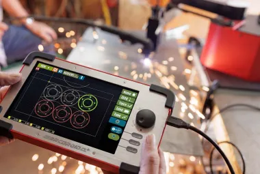 Hands holding the ArcDroid Plus controller with a touchscreen showing circle cut paths and a joystick, with plasma cutting sparks in the background