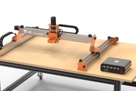 FoxAlien XE-Ultra 8080 CNC router with orange brackets and black drag chains mounted on a workbench, controller box sitting on the table beside it
