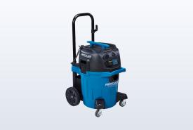 Blue and black HERCULES 12-gallon dust extractor on wheels with its hose attached, standing in a half-finished room