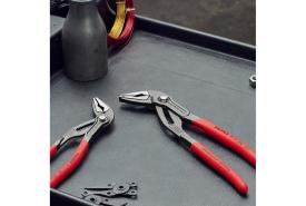 Knipex Cobra water-pump pliers with red handles lying on a dark tray beside small hardware