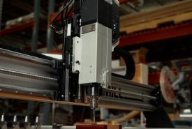 Sienci AltMill automatic tool changer spindle cutting a block of wood in a workshop, with the tool rack visible at the left