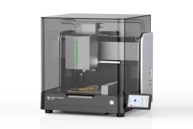 TwoTrees ED1 enclosed desktop CNC machine with a smoked glass cover, spindle and tool changer inside, a carved piece on the bed, and a touchscreen at the front right