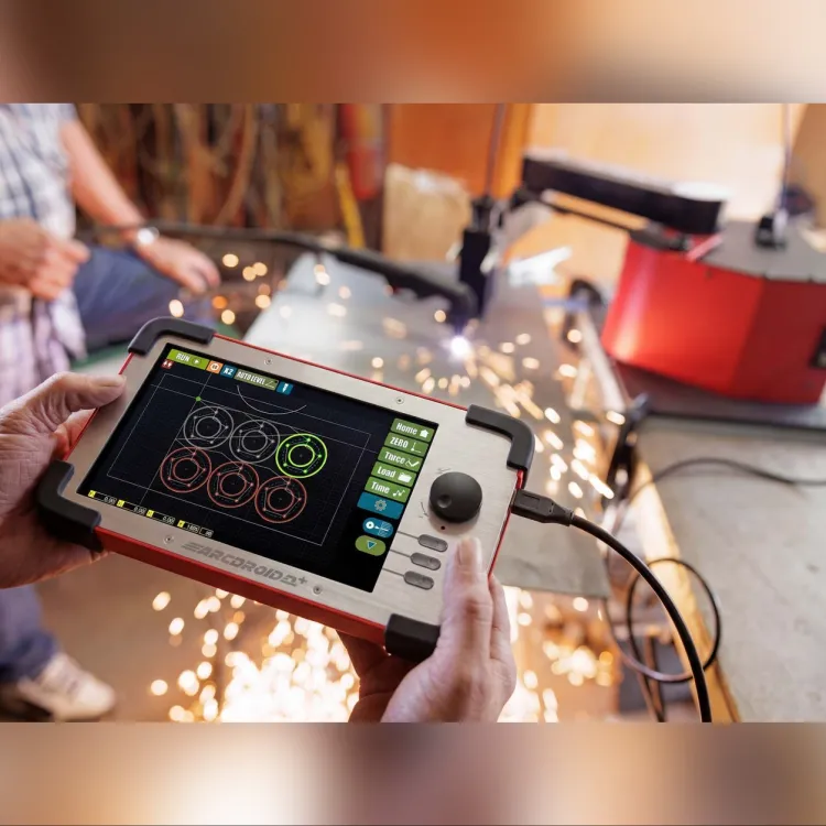 Hands holding the ArcDroid Plus controller with a touchscreen showing circle cut paths and a joystick, with plasma cutting sparks in the background