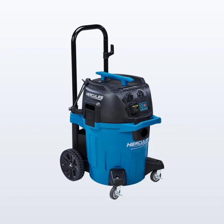 Blue and black HERCULES 12-gallon dust extractor on wheels with its hose attached, standing in a half-finished room