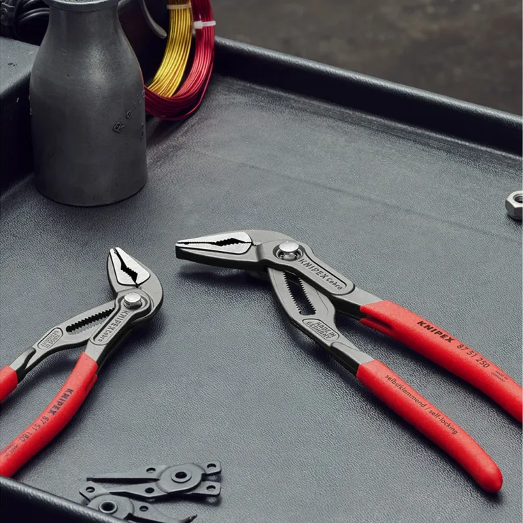 Knipex Cobra water-pump pliers with red handles lying on a dark tray beside small hardware