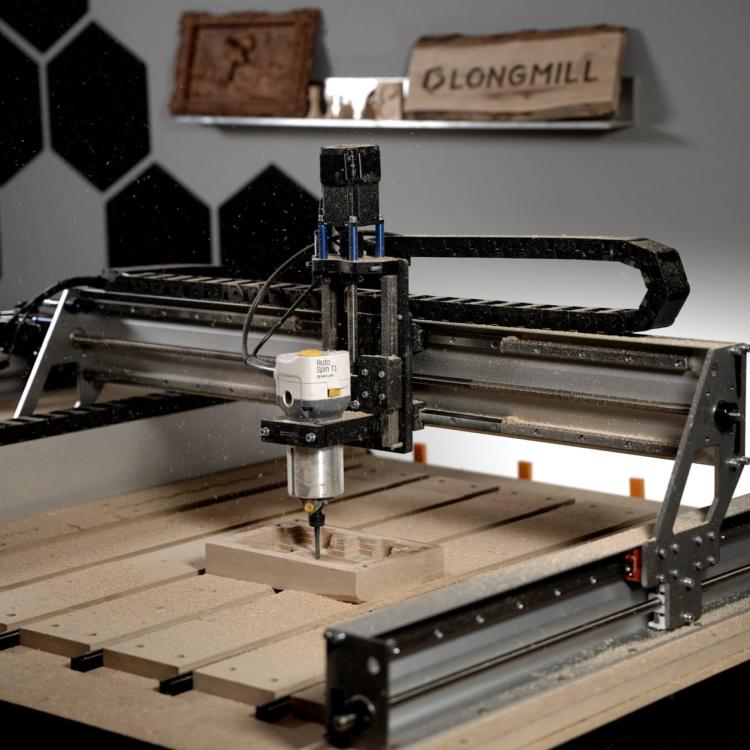 Sienci LongMill MK3 CNC router with a trim router mounted on the gantry, cutting a wooden part on a slatted table, with a LongMill sign on the wall behind
