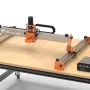FoxAlien XE-Ultra 8080 CNC router with orange brackets and black drag chains mounted on a workbench, controller box sitting on the table beside it