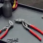 Knipex Cobra water-pump pliers with red handles lying on a dark tray beside small hardware