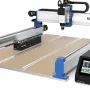 Genmitsu PRONAX CNC router with blue end plates, a silver gantry, a perforated bed, and a black touchscreen controller at the front right