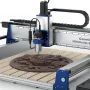 Fully assembled Genmitsu PROVerXL 2×2 CNC router with a blue and silver frame, a spindle above a slatted table holding a carved round relief, and the controller box at the front right